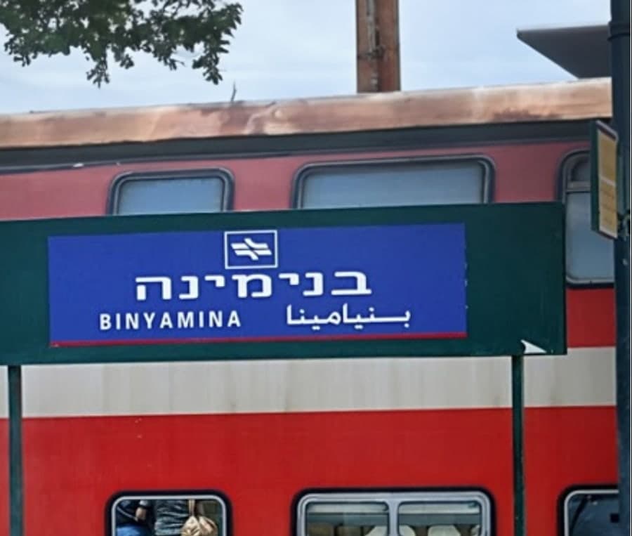 שלט תחנת הרכבת בנימינה על רקע קרון רכבת אדום